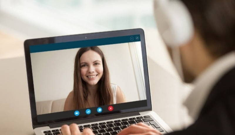 Man with headphones and laptop speaking to women over video chat